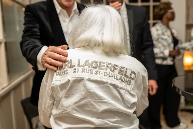 Mémé di spalle, con la sua camicia bianca Karl Lagerfeld, abbracciata da un ospite